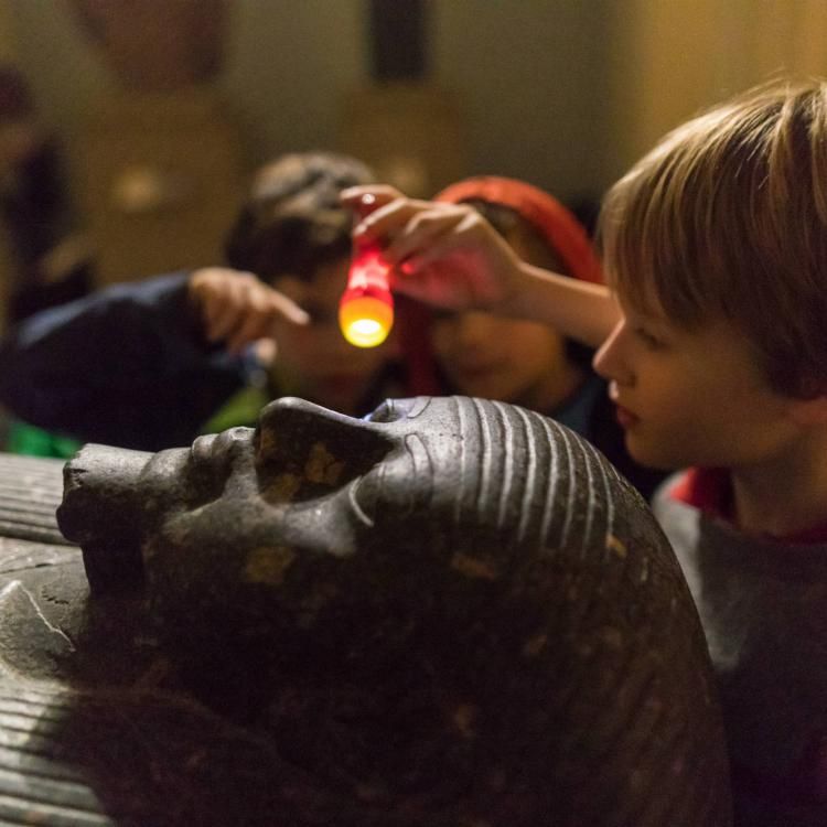 Children looking at an Egyptian sculpture in torchlight at a Museum sleepover.