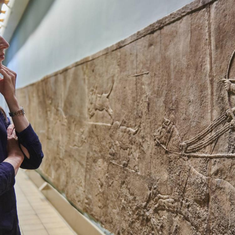 Woman looking at wall panel relief depicting Assyrian lion hunting