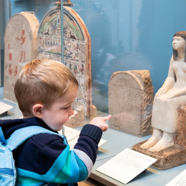 A child and his grandmother looking at the limestone statue of Nofretmin in Room 62-63