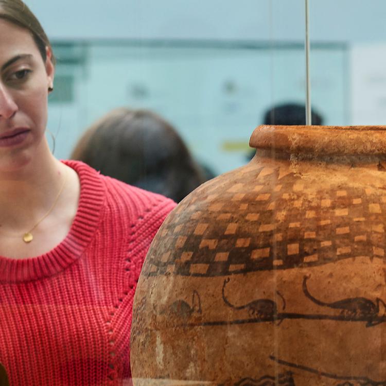 A woman observes a decorated jar which has been painted with square shapes and scorpions