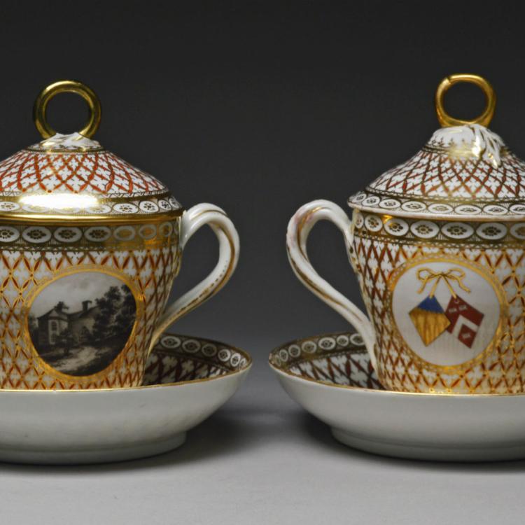 Two patterned porcelain cups with lids and a saucer.