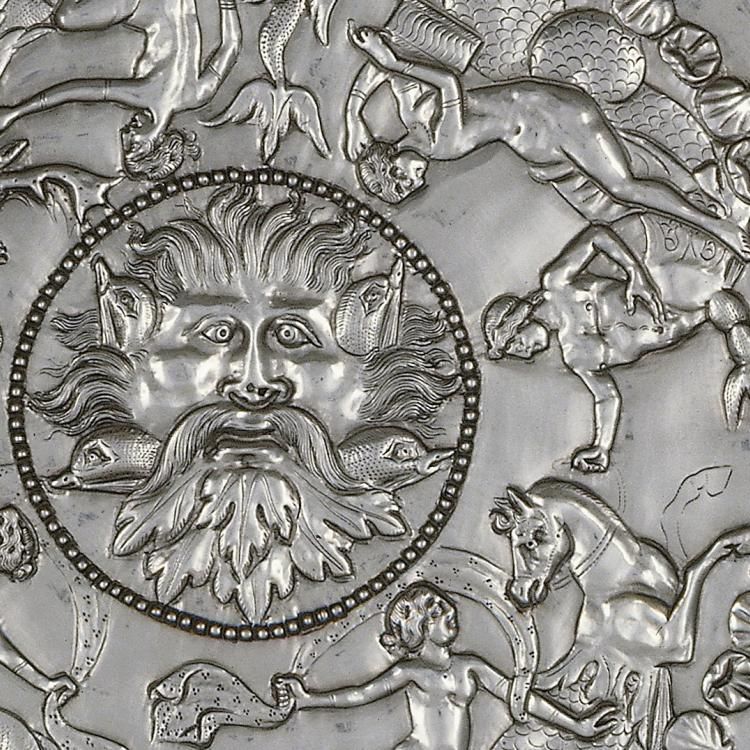 Close up of silver dish, covered with mythical beings and face