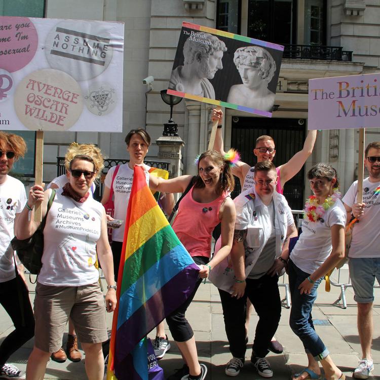 Members of Museum staff pose with a rainbow flag and placards showing British Museum objects