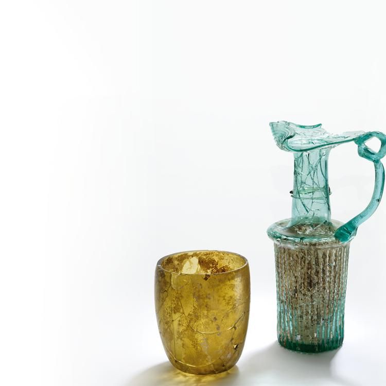 Two glass objects, a cup and a vase, sit in front of a white background. There appears to be some marks on the objects.