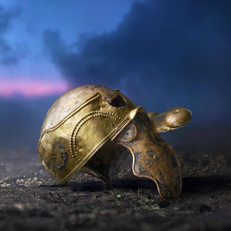 Bronze helmet lying on the earth, mostly intact but with the crest box, one cheek-piece and several of the bosses missing.