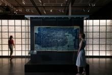 Visitor standing to one side of a central display case looking at a large monochromatic map on display within.