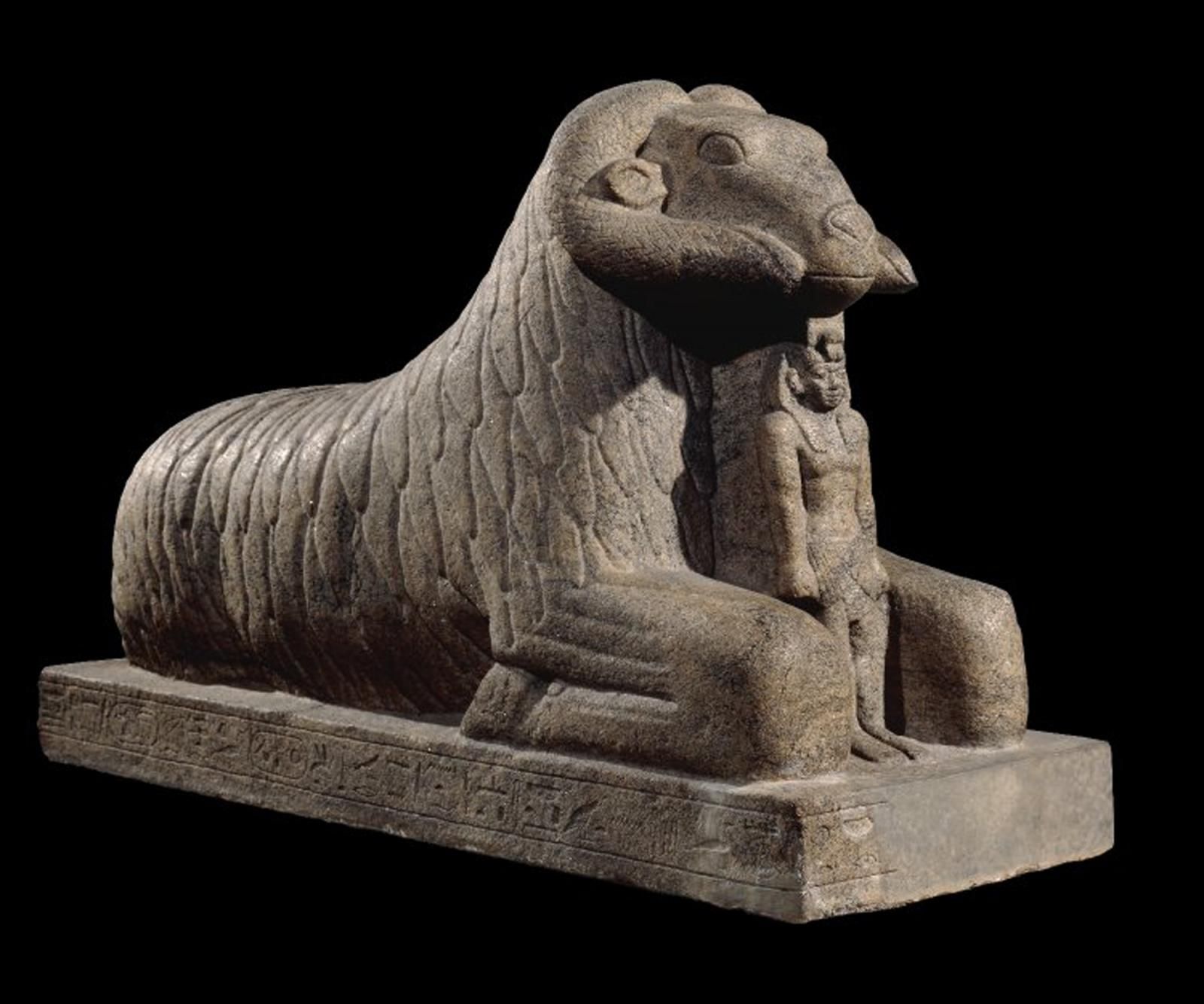 Granitic figure of a pharaoh between folded legs of a larger ram sphinx.