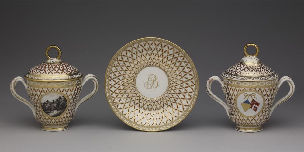 Pair of chocolate-cups, covers and saucer with twisted handles and ground diapered with network of gold and red