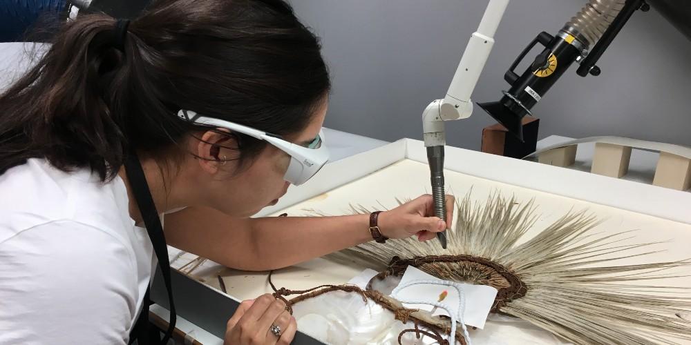 Woman wearing safety goggles cleaning a shell headdress with a laser. 