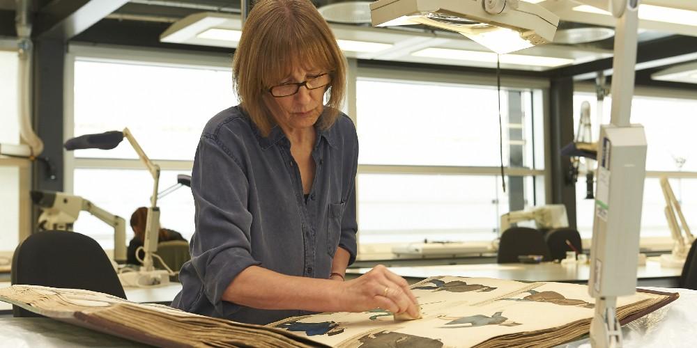 A woman working on a large bound book. 