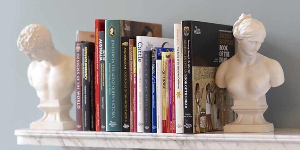 A selection of books on a mantlepiece in between two bust bookends. 