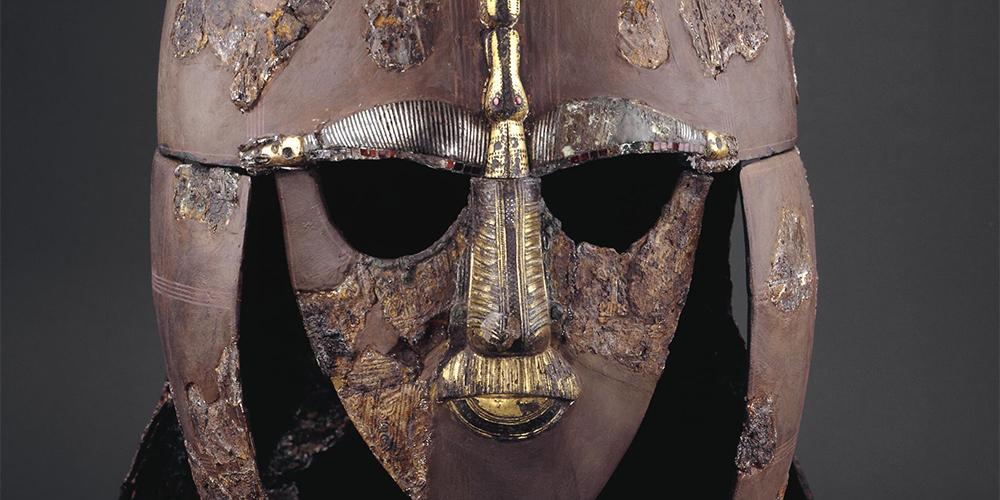 Close up of iron and tin-bronze helmet, with eye holes and gold features on the nose and lips.