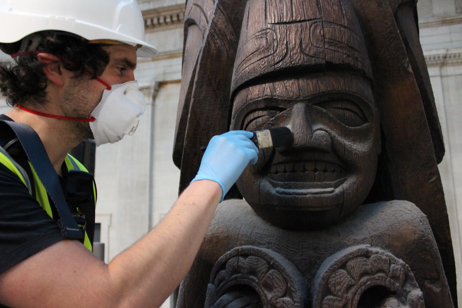 Conservator Jamie Hood removing dust from the Haida totem pole in the Great Court.