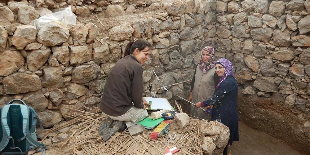 Three archeologists standing in a archeological site recording data.