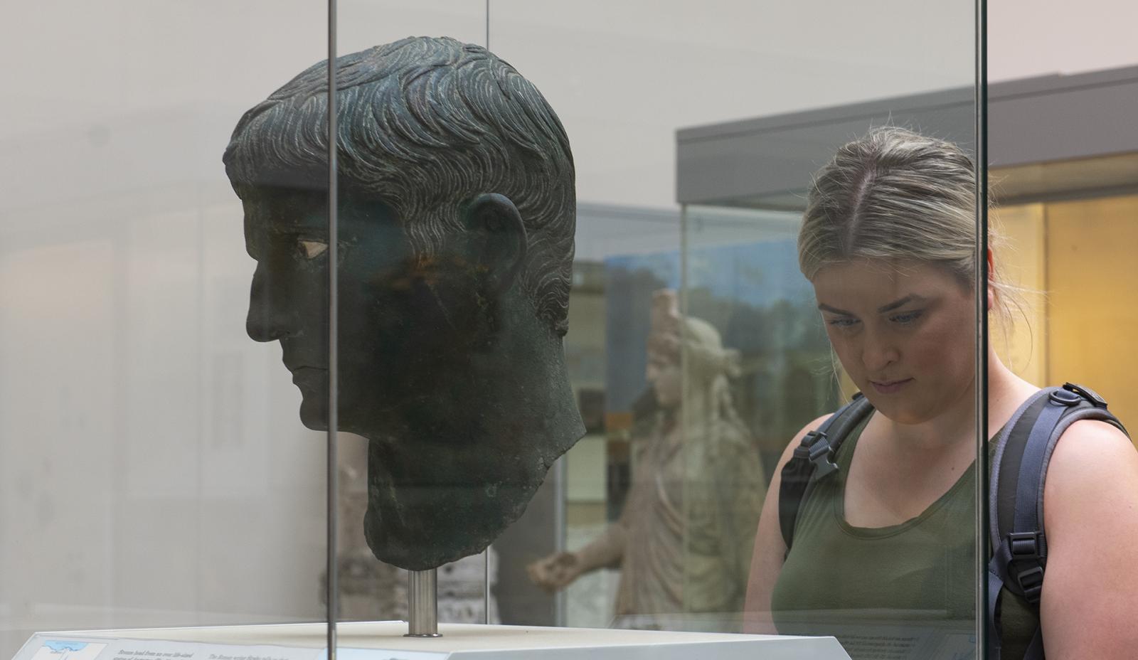 Visitor standing in front of a statue of a Roman head.