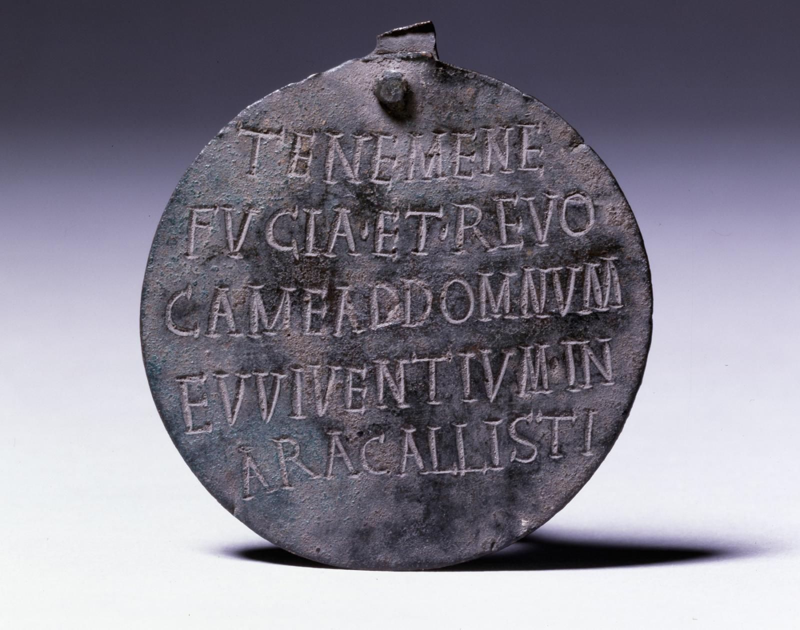 A small metal plate with five lines of Latin writing on it.