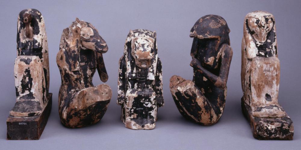 Five wooden figures including a seated ram all with patches of black resin. 