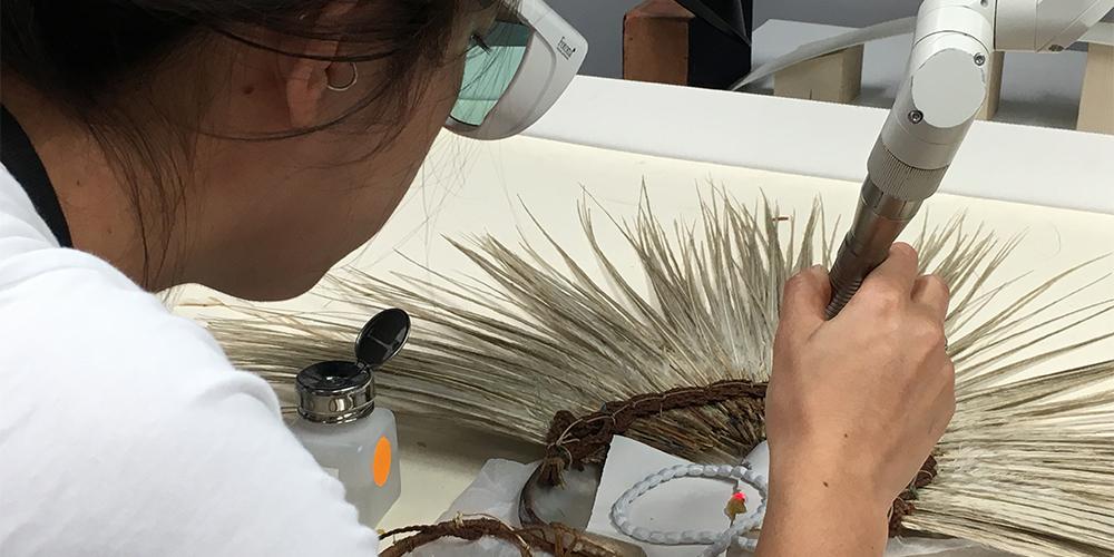 Scientist using a laser to clean a headdress.