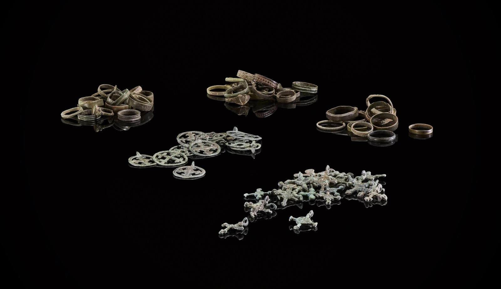 Five groups of metalwork, including rings and broaches, sit on a black background. Each group displays the same objects, around 10 in each group.