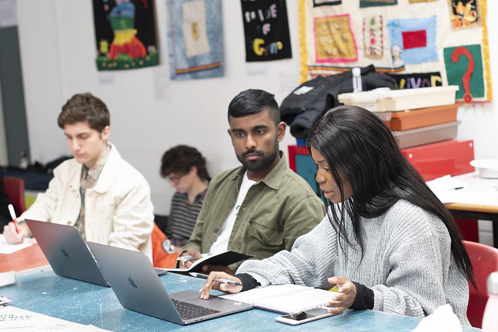 Three young people at a desk with laptops during a workshop.