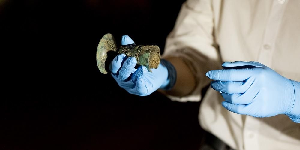 A person wearing blue gloves carefully holds a ancient cup.