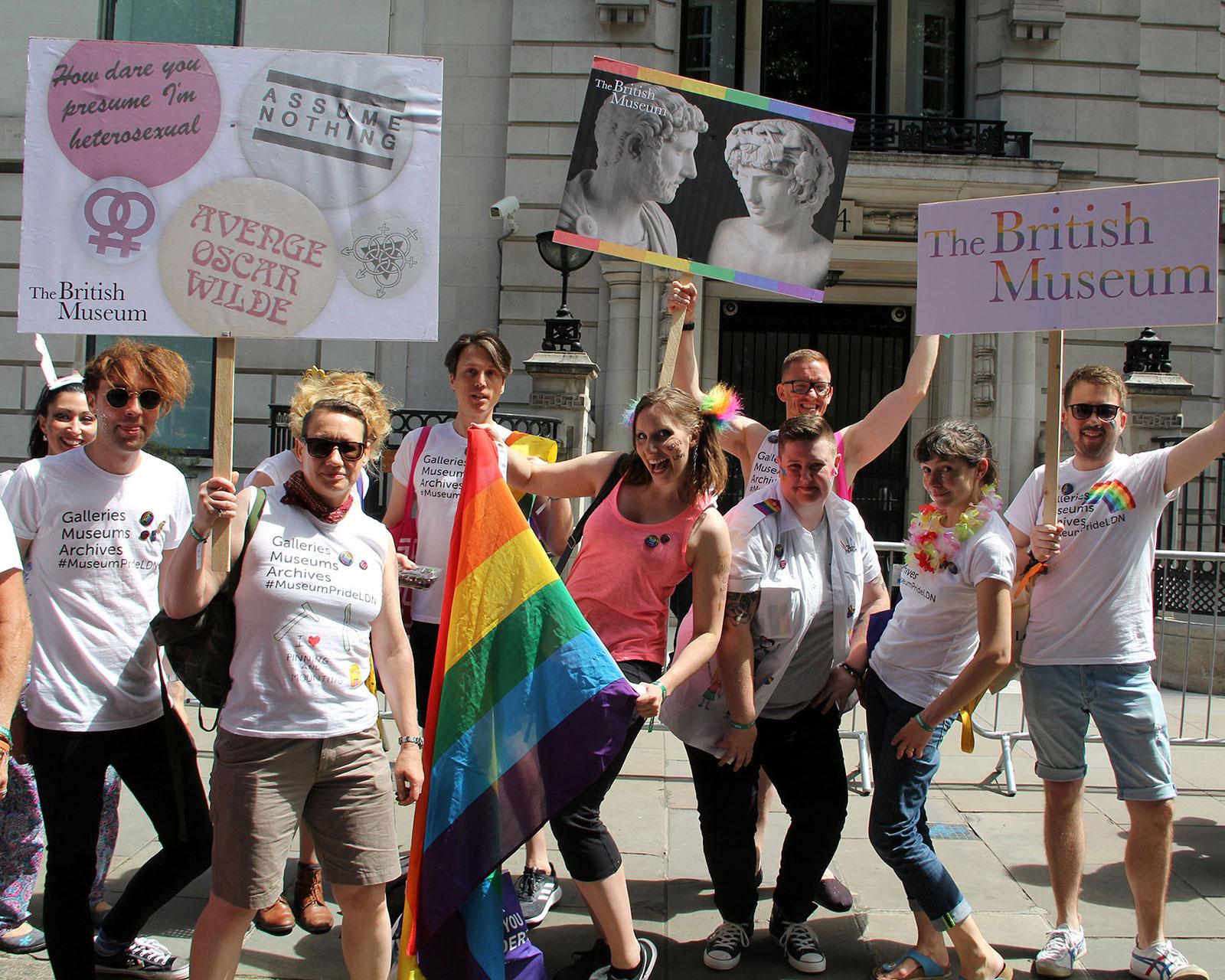 Members of Museum staff pose with a rainbow flag and placards showing British Museum objects