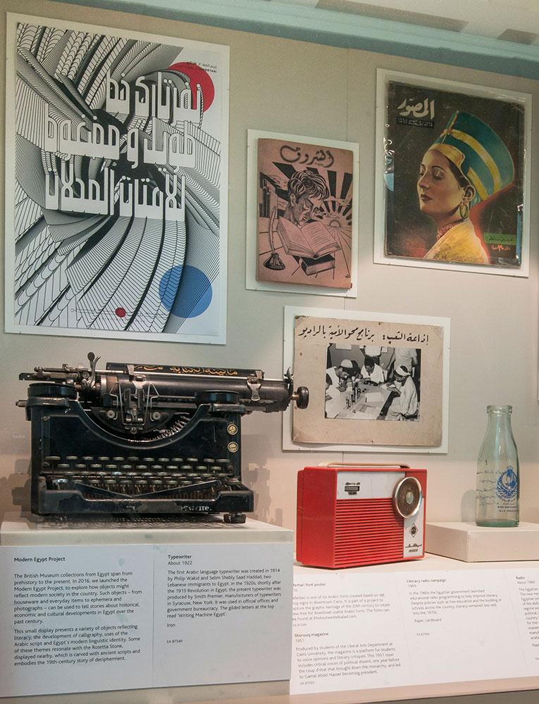 Objects in a display case including a typewriter, a transistor radio and a glass bottle