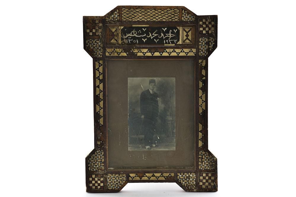 Photo of the Ahmed Muhammad Chahine, wearing a fez and suit and holding a staff, in an elaborate wooden picture frame.