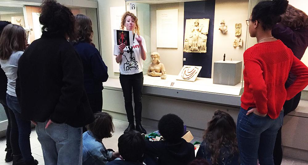 An educator speaks to a group of school children whilst standing in front of a relief