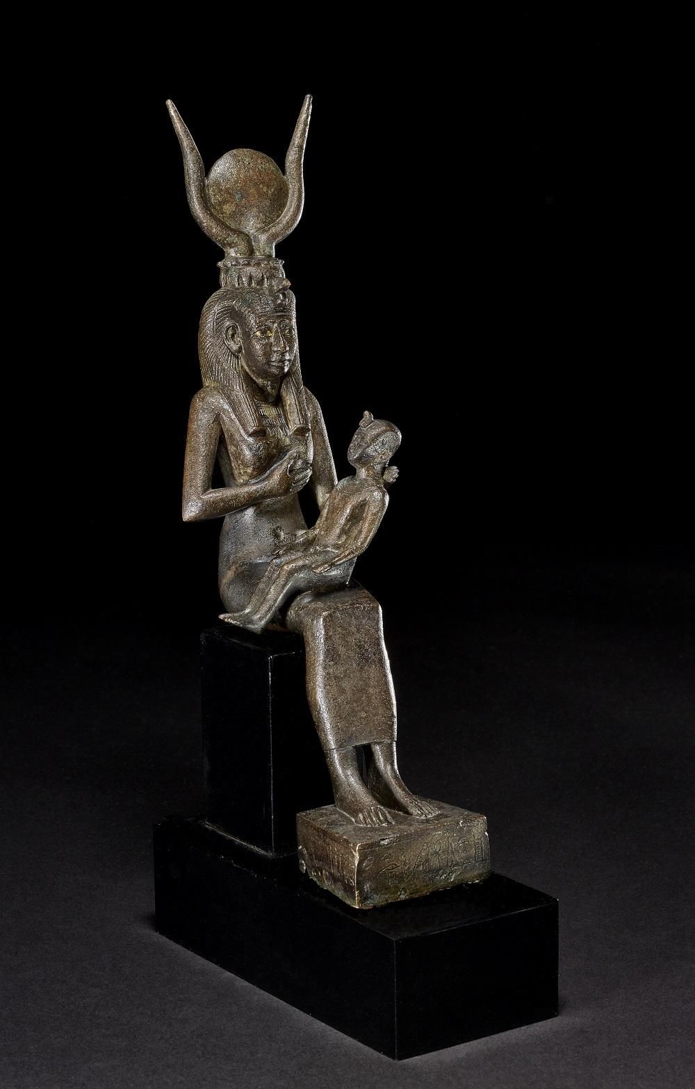 Bronze statue of the Isis, with her young son Horus on her lap. She is holding her left breast and aiming it towards her baby, while he stares into the distance.