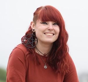 A photo of Olivia, who is smiling and has bright red hair and is wearing a red top and large earrings.