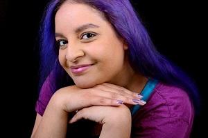 A photo of Raegan, who has bright blue-purple hair and is wearing a pink-purple top.