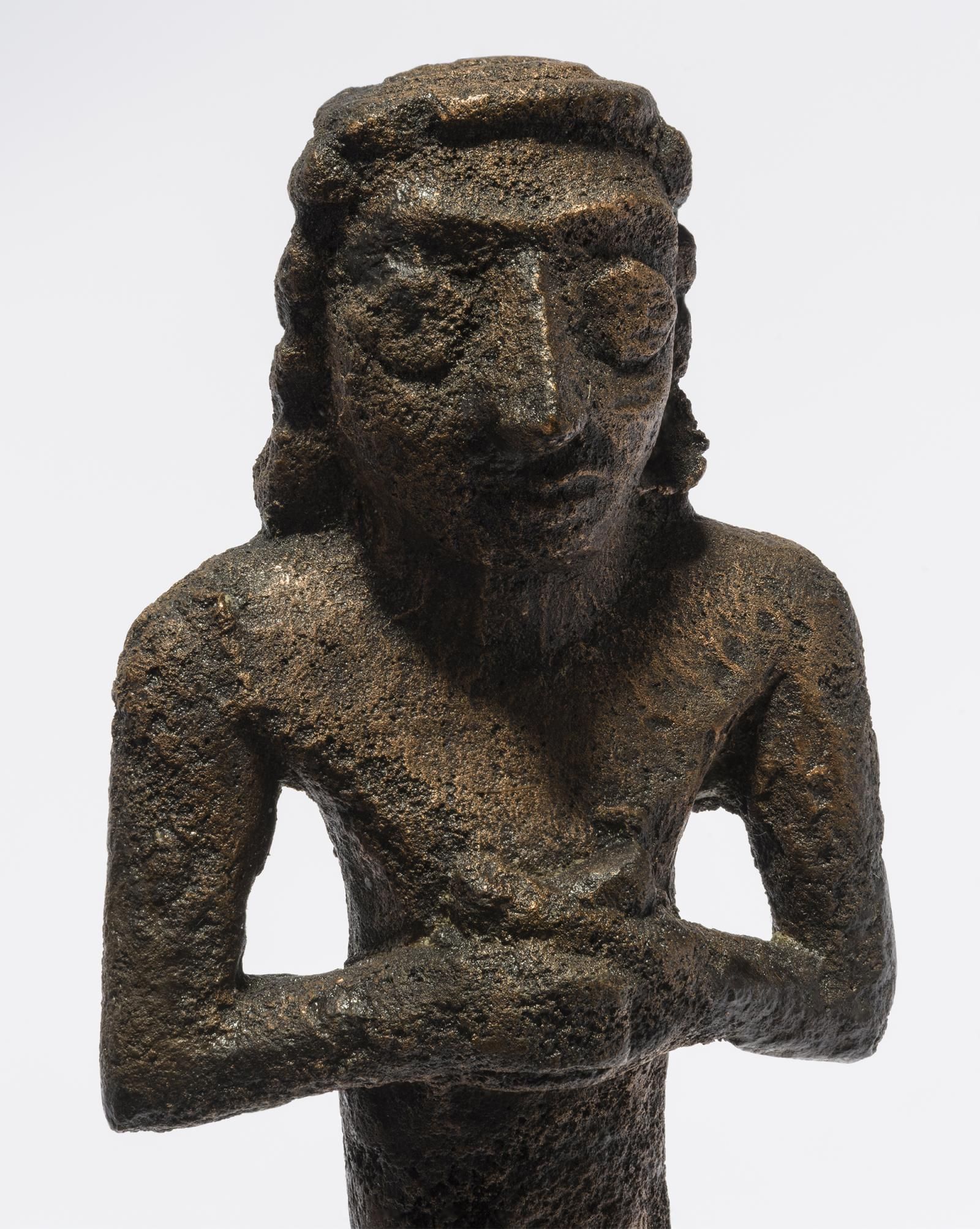 Copper alloy figure with a face and clasped hands.