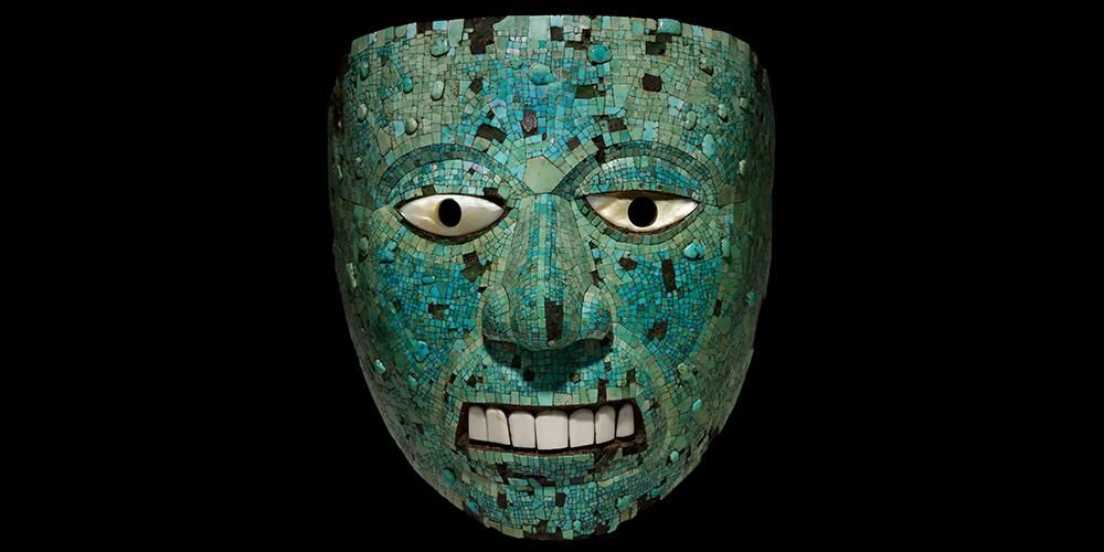 Mask in the shape of a human face formed of tiny intricate turquoise mosaic pieces and individual larger white pieces to represent the eyes and teeth. The smaller turquoise pieces follow the contours of the face although some appear to be missing and some areas of the mosaic are slightly discoloured.