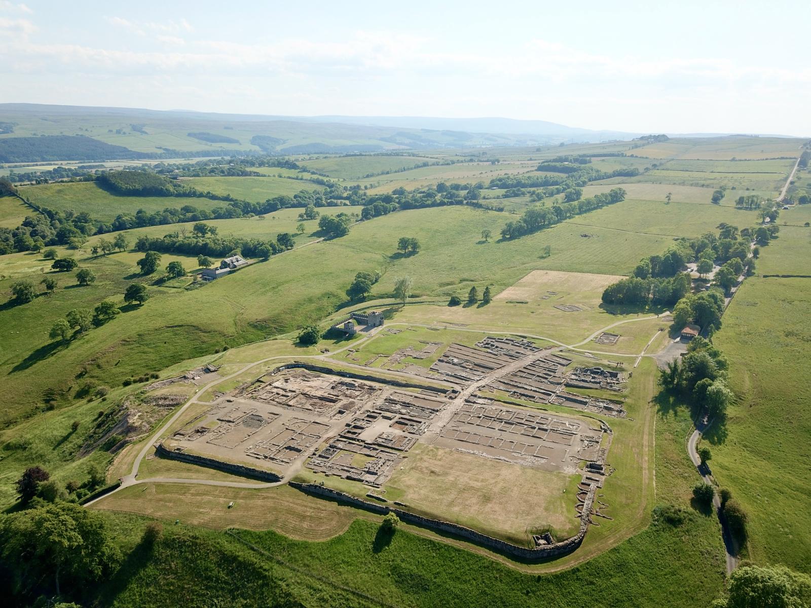 Aerial view of Vindolanda site under excavation, on a bright day amid green rolling hills