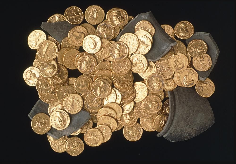 A pile of gold coins with the head of an emperor embossed on them, against a black background