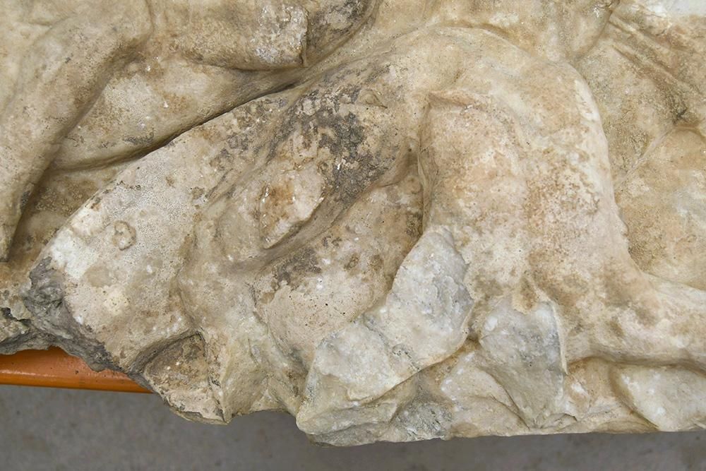 Detail of a stone relief showing a man being crushed by a horse. The stone is clean and bright in places and dark and discoloured in others.