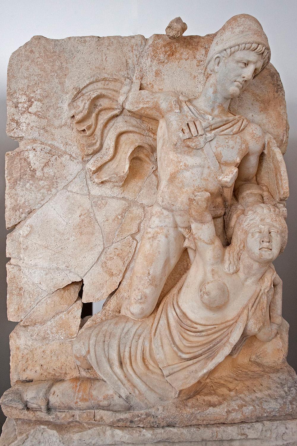 A man in Roman military uniform stands over a female warrior and holds her to the ground