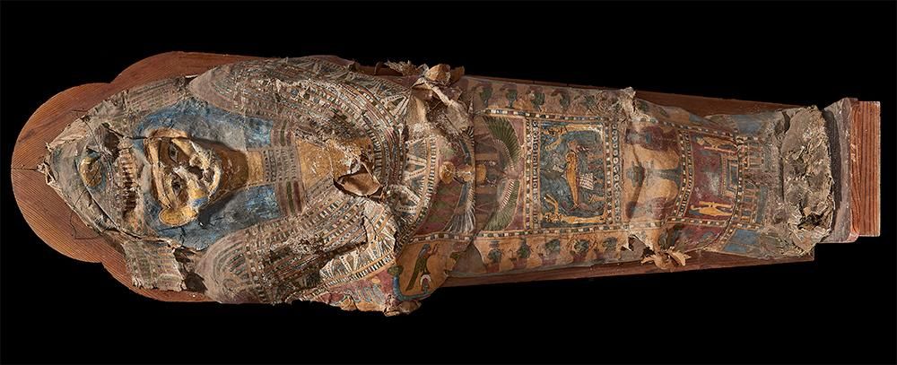 A coffin made of cartonnage material and painted with hieroglyphs and a human form. The cartonnage is damaged and has collapsed in multiple places