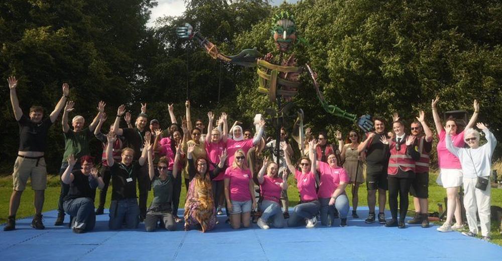 A crowd of people stood in a park cheering with their hands in the air.