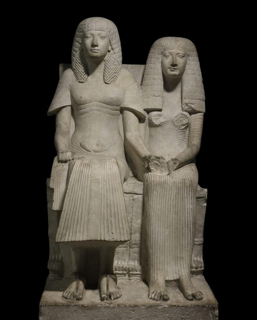 Statue of Horemheb and Amenia seated on chairs with lion-paw feet. Damage to chest and hands of Amenia.